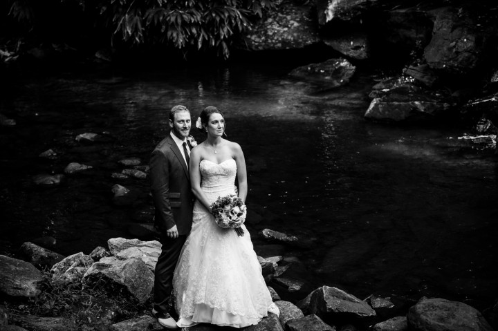 Adventurous couple poses on their wedding day on the rocks by the stream at Montreat College