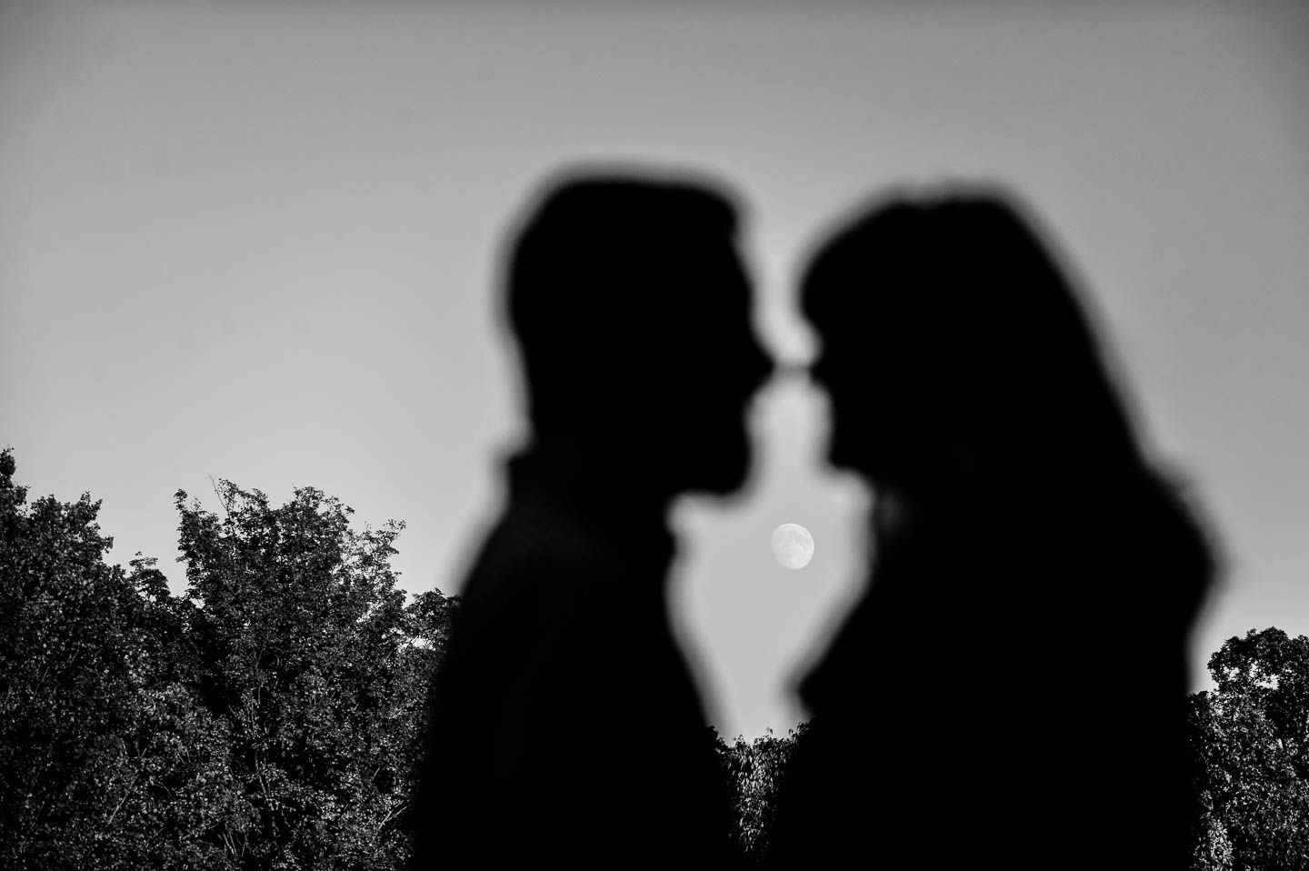 Silhouette of a wonderful couple  on top of a hill in black and white with the moon framed between them
