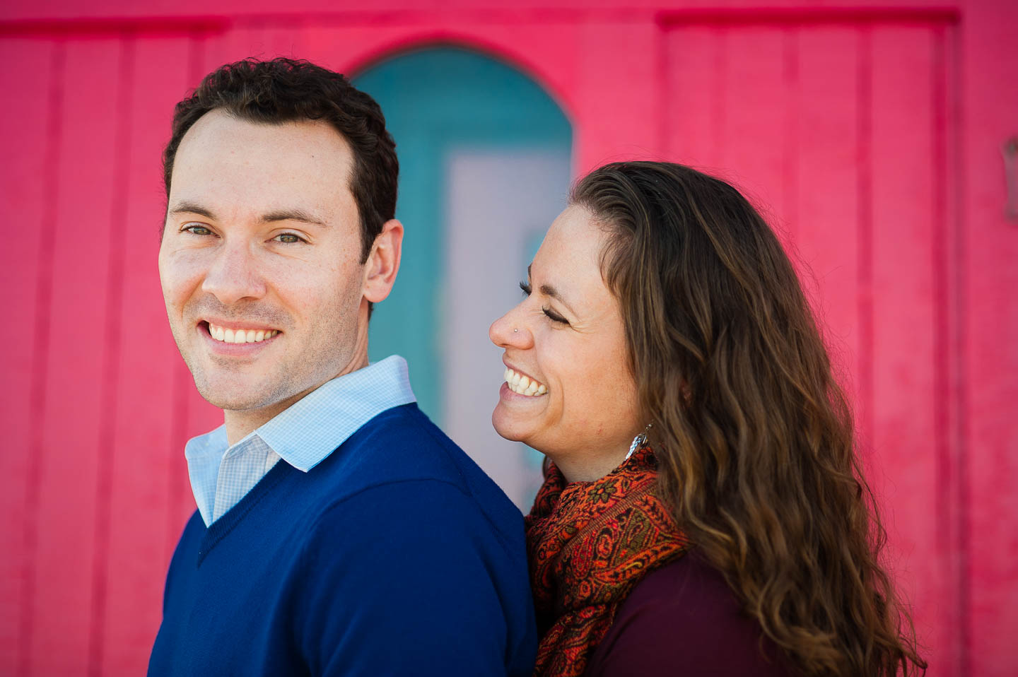 Attractive couple posing in front of a vibrant red barn board wall on Cape Cod during there engagement session