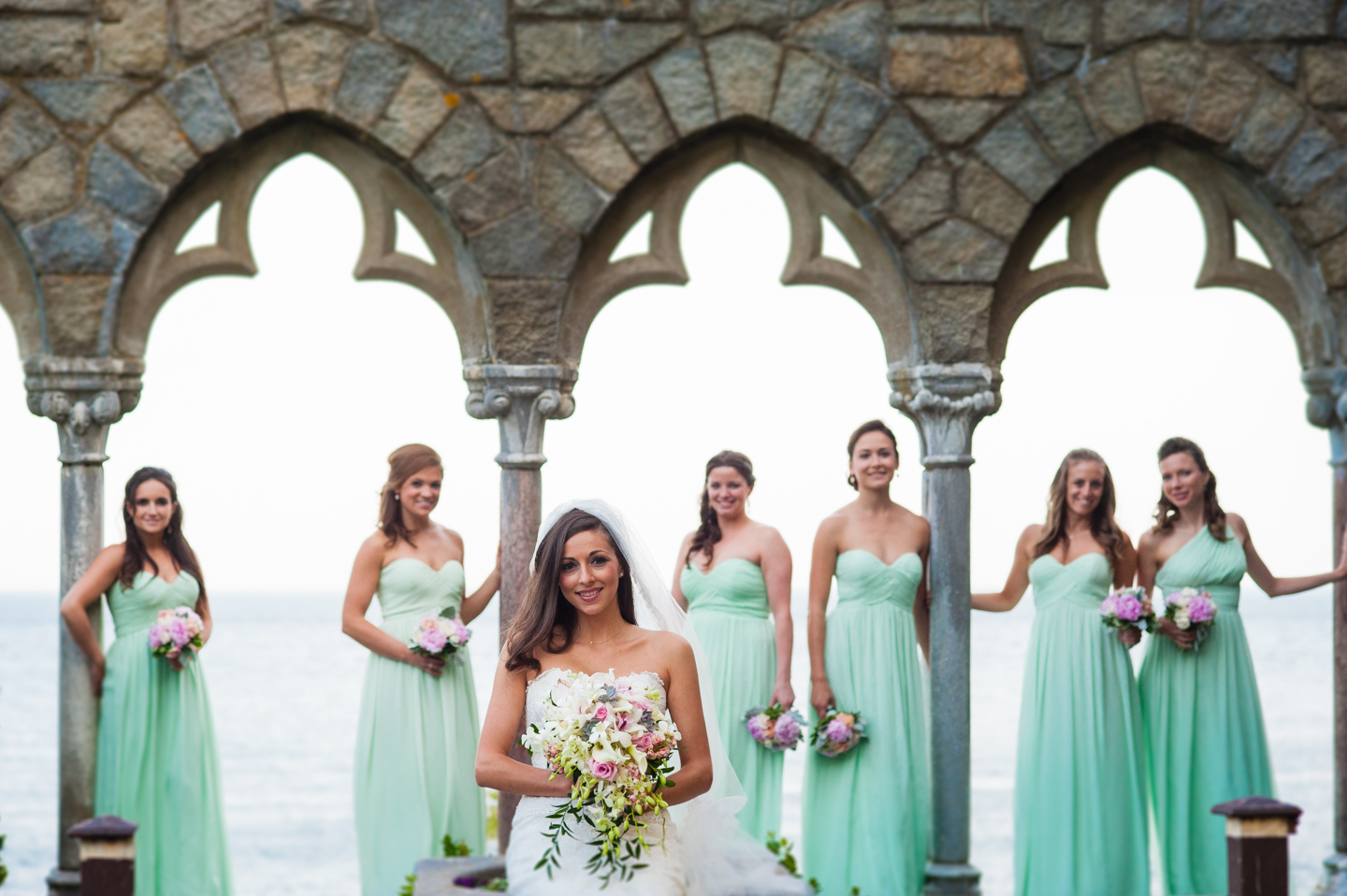 Beautiful bride and her bridesmaids pose for a portrait  by some stone arches at Hammond Castle