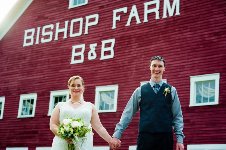 Bride and Groom pose in front of red barn during their rustic wedding at Bishop Farm 