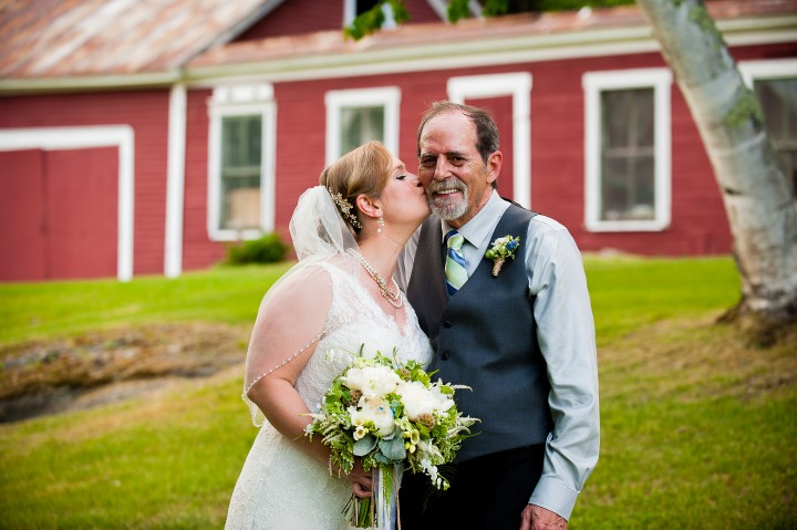 Bride gives her dad a quick kiss on the cheek during pictures at her farm wedding 