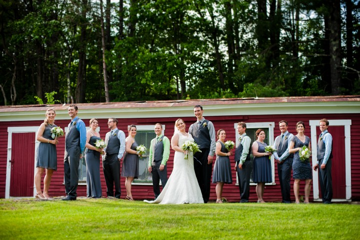 beautiful wedding party poses in front of a red barn for a quick group photo 