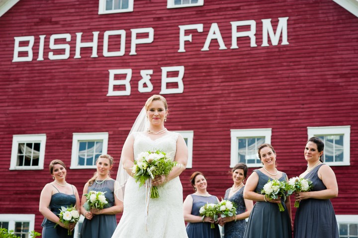 bride and her beautiful bridesmaids pose in front of big red barn