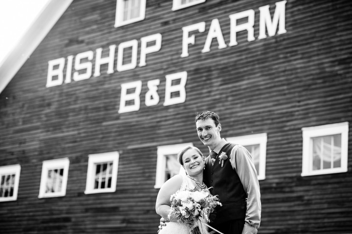 Bride and groom pose smiling at the camera during their barn wedding reception