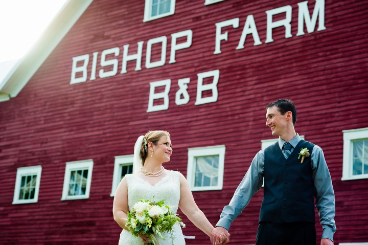 bride and groom hold hands and look at each other in front of red barn 