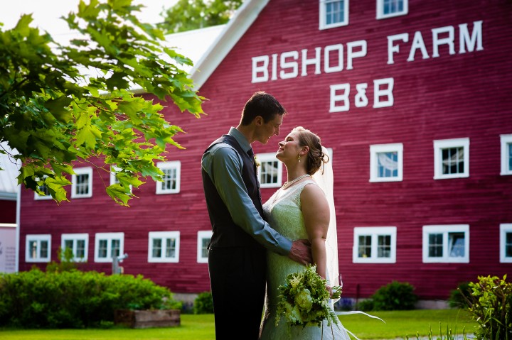 bride and groom embrace in front of beautiful red barn during their farm wedding