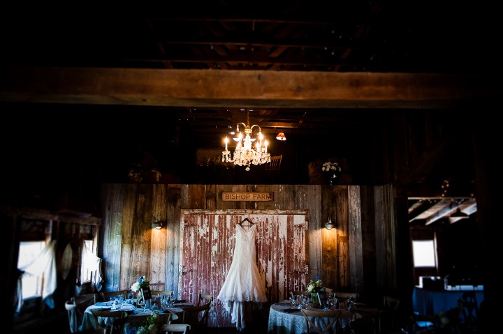 The brides lace wedding gown hangs in a barn for a pre-dressing image 