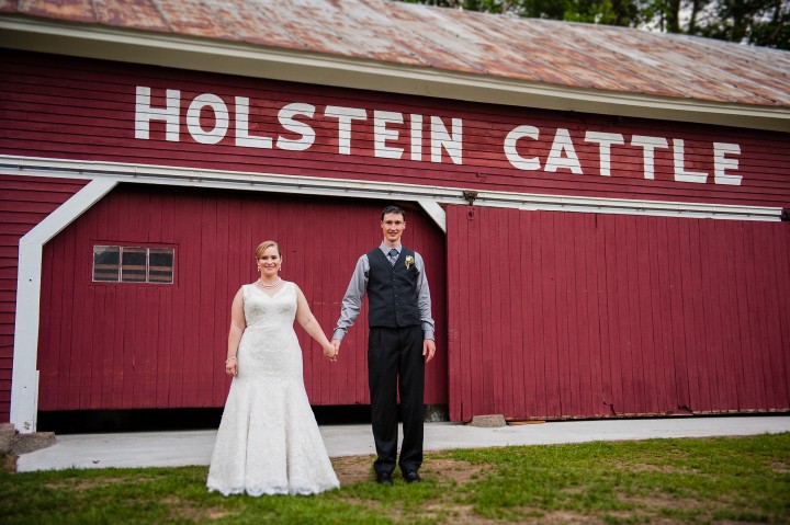 Bride and groom pose in front of old cattle barn during their rustic wedding reception 