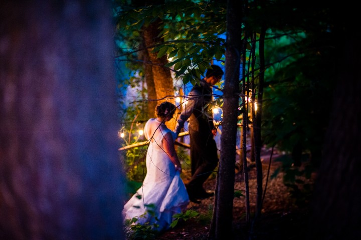 groom leads his beautiful bride down a christmas tree light wooded path 