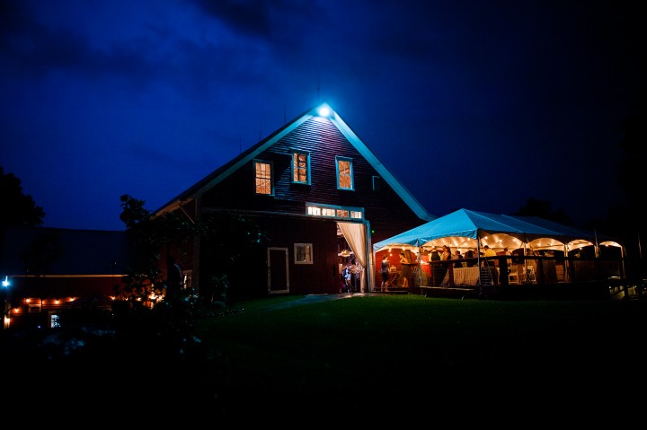 lightning lights up the sky behind the barn during bride and grooms wedding reception