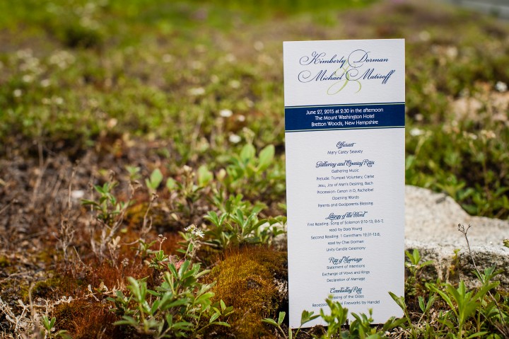 White and blue wedding ceremony programs rest on the mountain vegeation 