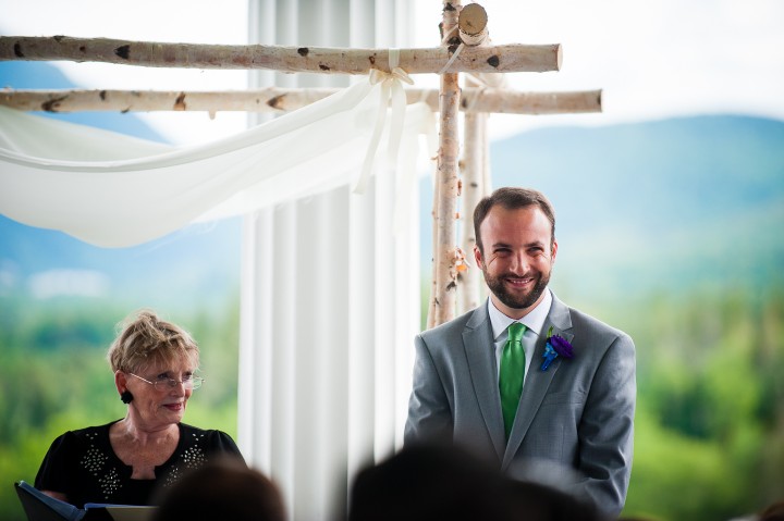 a very happy groom watches his bride walk down the aisle at the start of his luxury mountain wedding 