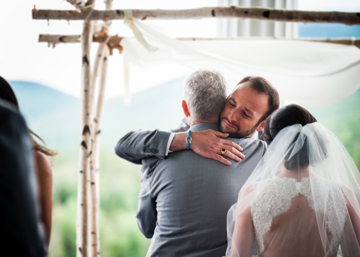 handsome groom hugs the brides dad at the start  of his mountain wedding ceremony