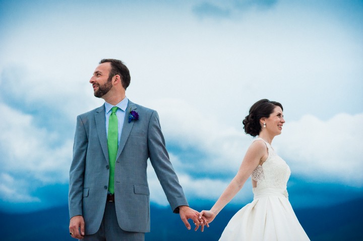 Bride and Groom hold hands with the sky and mountains behind them on their Mount Washington Wedding day 