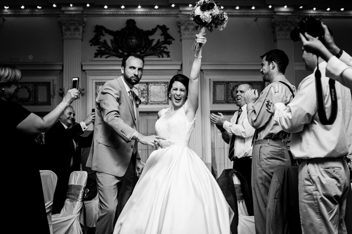 a very exuberant bride and groom cheer as they enter their wedding reception for their first dance as husband and wife