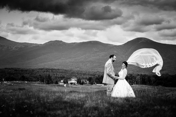 Gorgeous bride and her groom stand in a field with the brides veil blowing in the wind