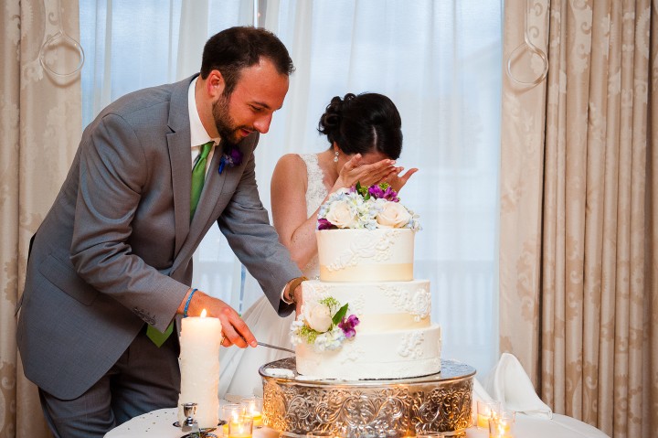 the bride covers her face as her groom attempts to cut the wedding cake during their mount washington hotel wedding reception