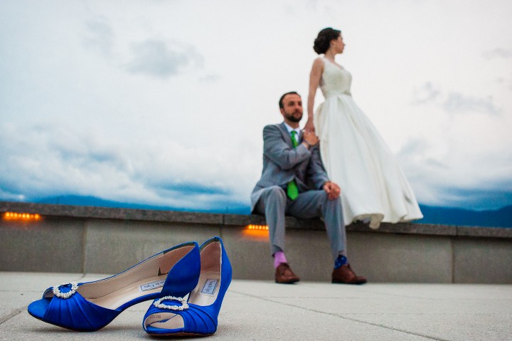 the brides beautiful blue wedding shoes in the foreground while the bride stands in the background with her handsome groom