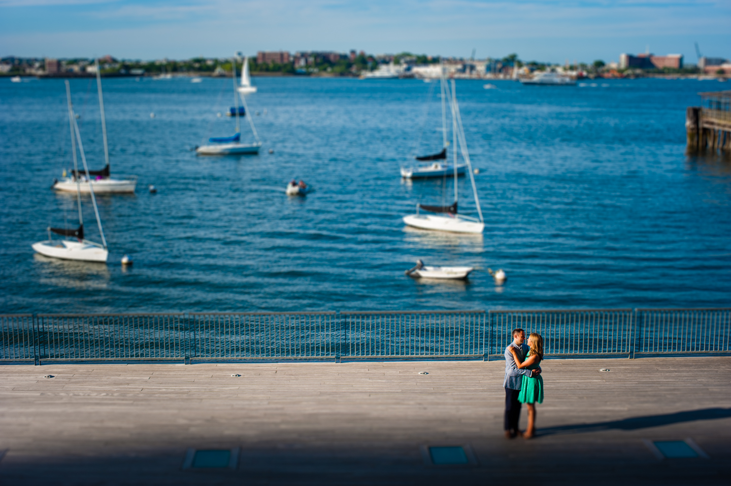 engaged couple embraces by the waterfront with a harbor full of boats behind them 