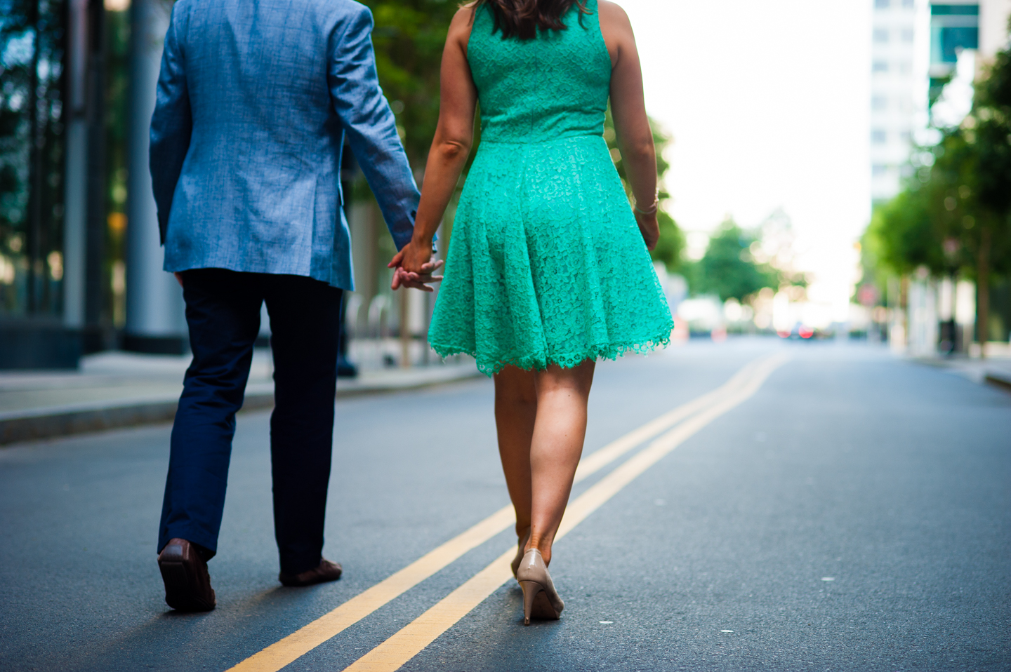 recently engaged couple holds hands and walks down the yellow line of a side street 