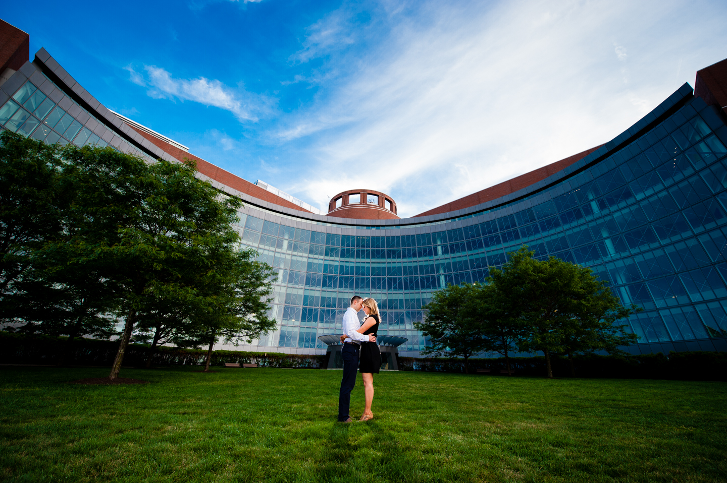 Couple embraces in front of gorgeous glass front building during their sunset engagement session