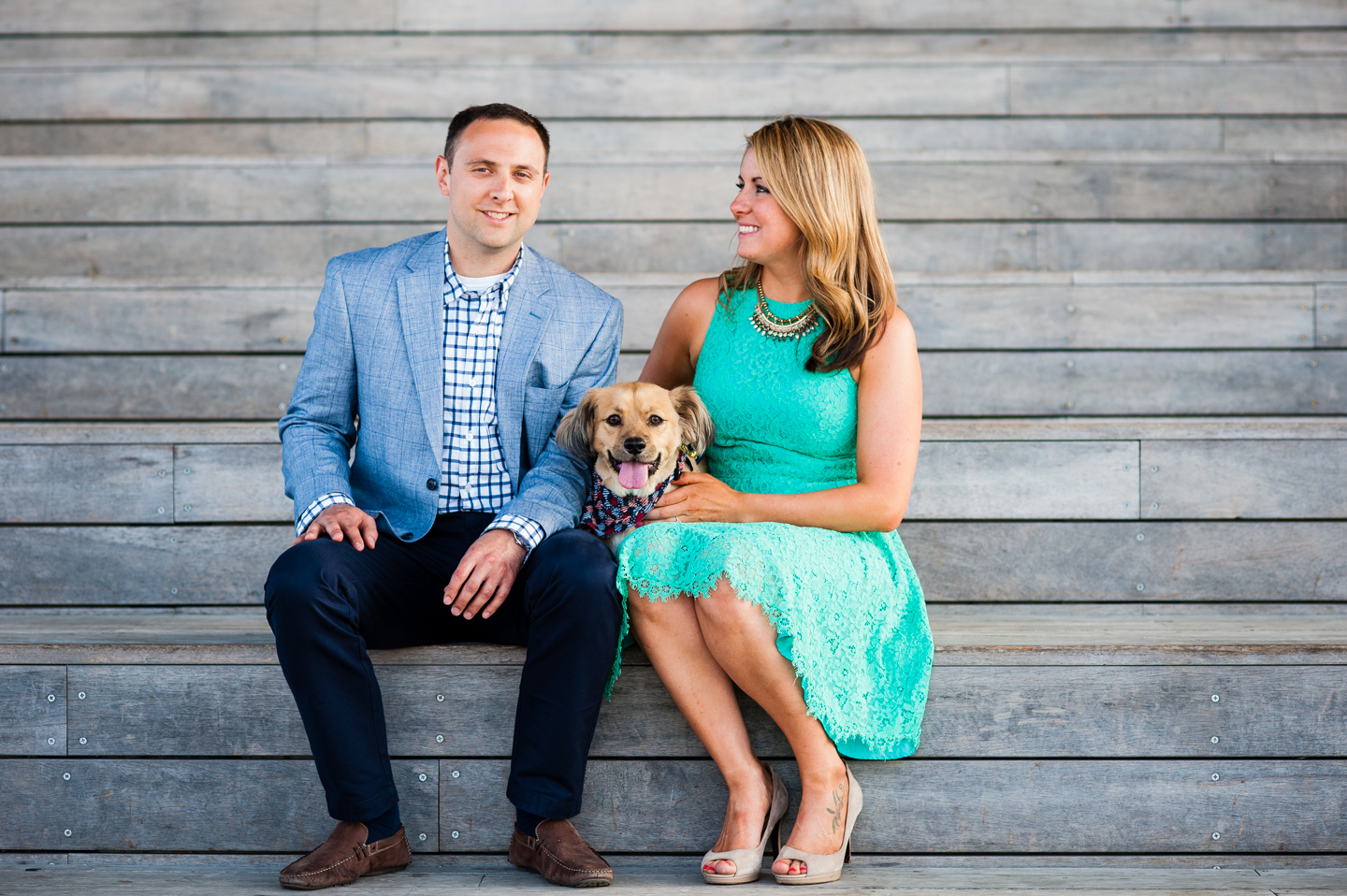 adorable engaged couple sits with their puppy on wooden stairs 