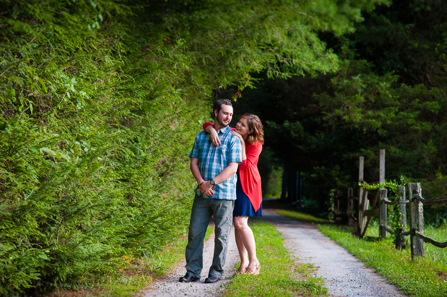 bride looks up at her groom as they pose along a wooded gravel driveway 