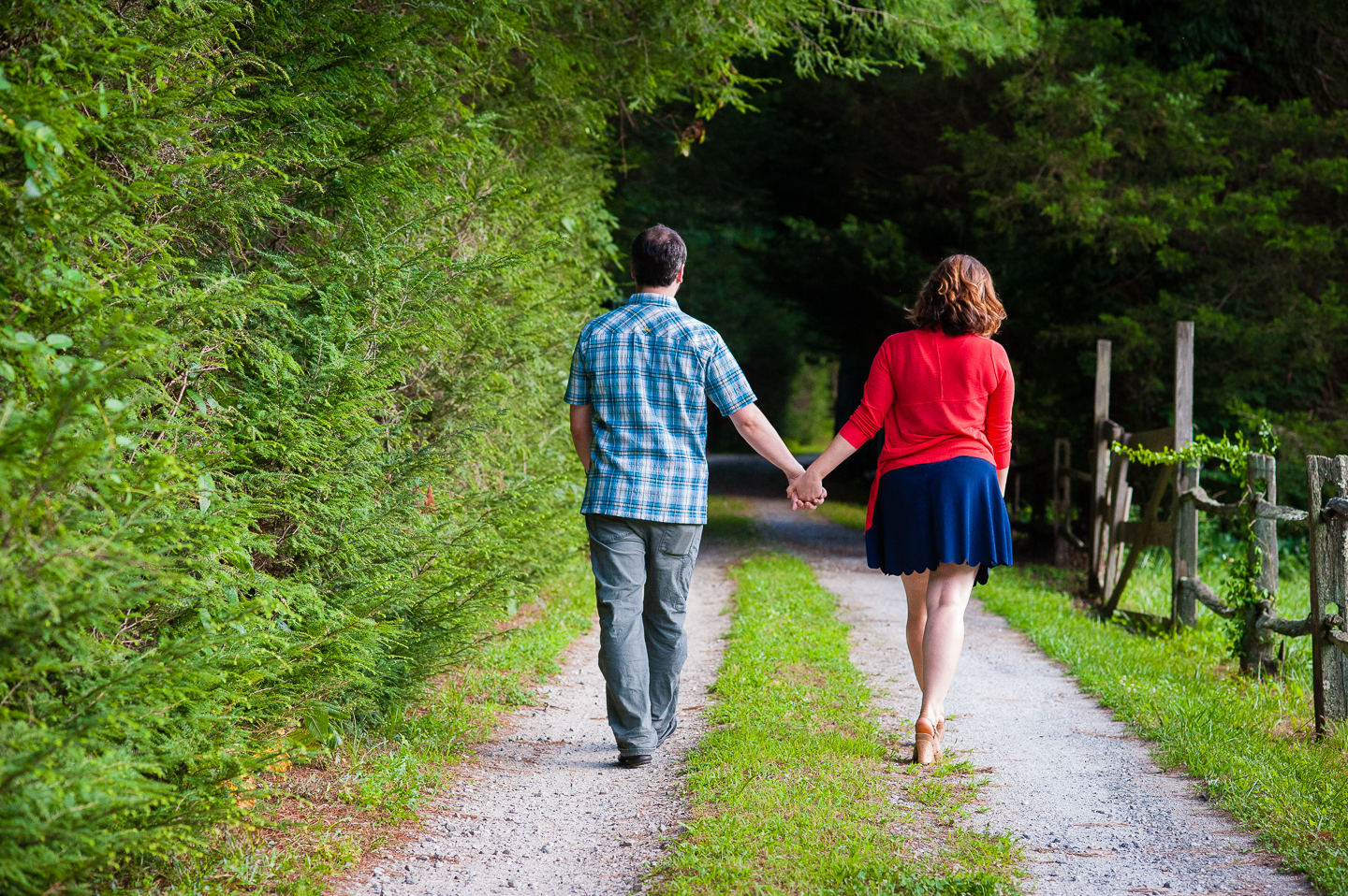 bride and groom hold hands and walk along a beautiful green driveway 