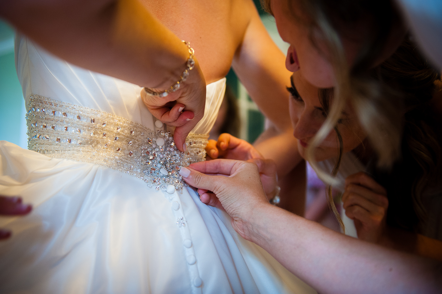 helping hands fasten the last few buttons on the brides gorgeous wedding gown