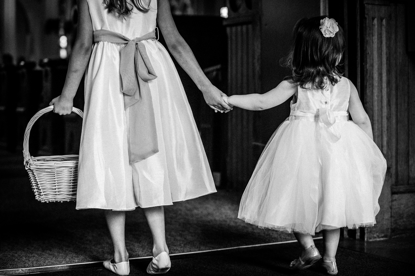 two adorable flowers girls hold hands as they begin to walk down the aisle