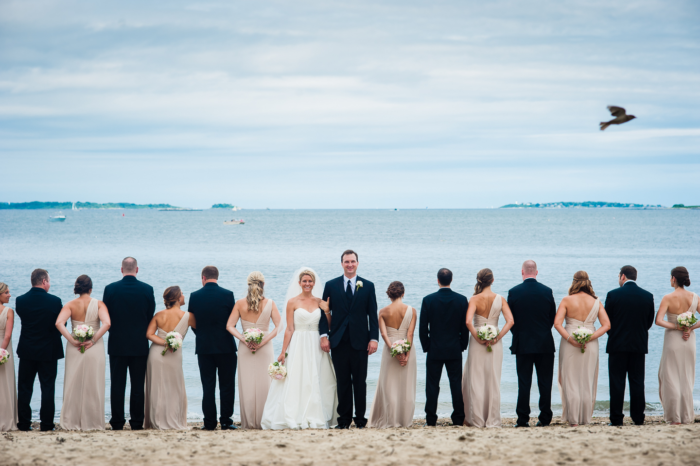 the bride and groom face the camera while the gorgeous wedding party faces the ocean  during this creative wedding party image 