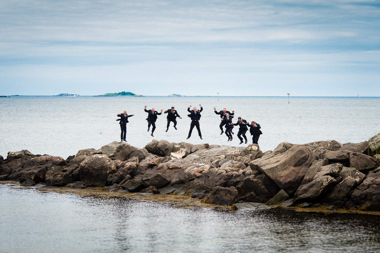 the groom and his groomsmen jumping on some ocean rocks 