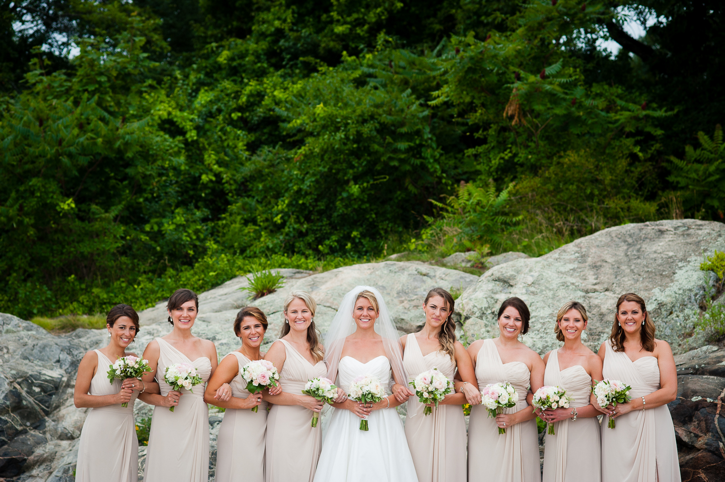 the bride and her gorgeous bridesmaids standing in front of a big rock 