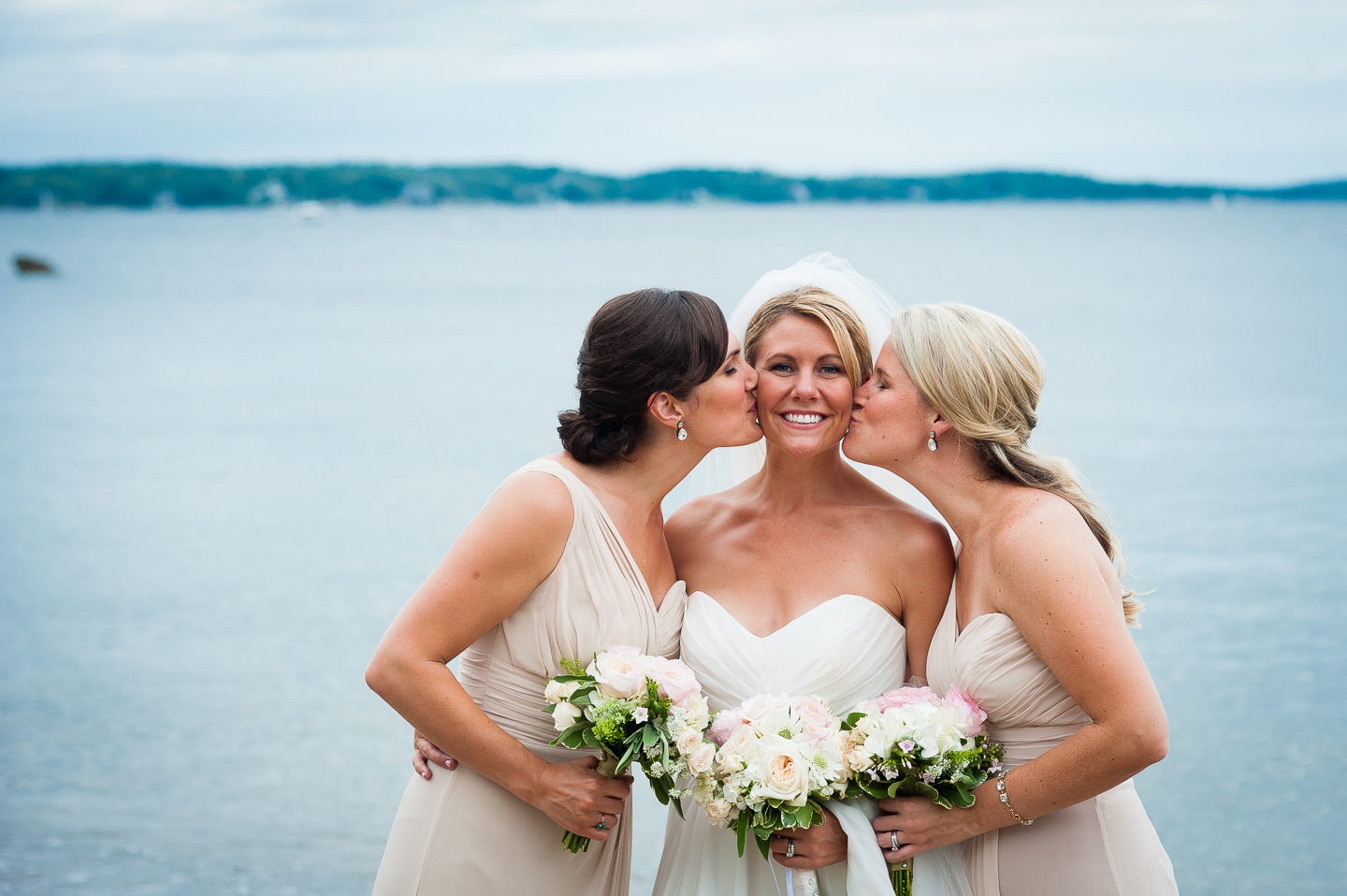 the brides two sisters give her a kiss on the cheek 