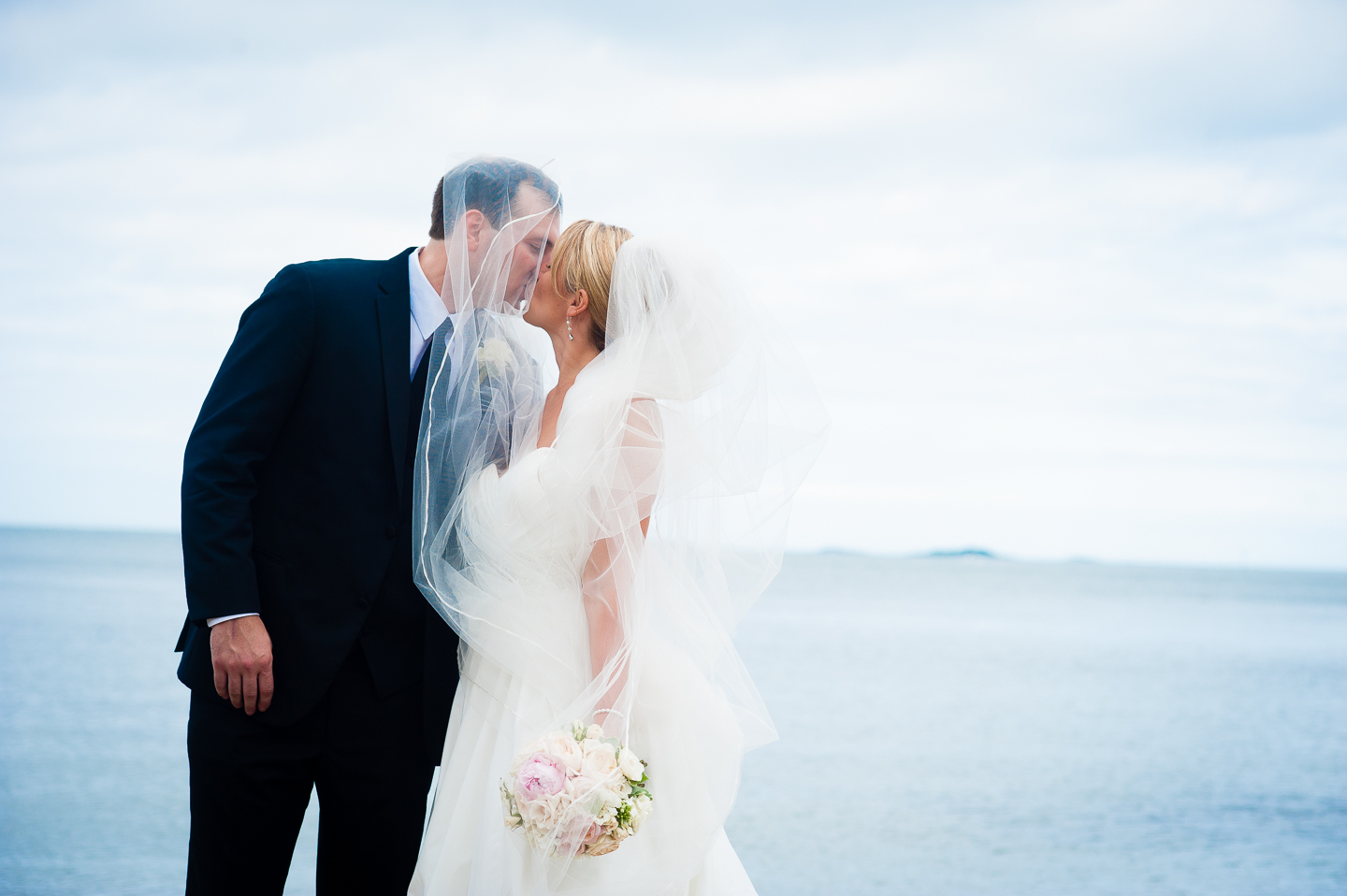 the groom wrapped in brides veil by the ocean 