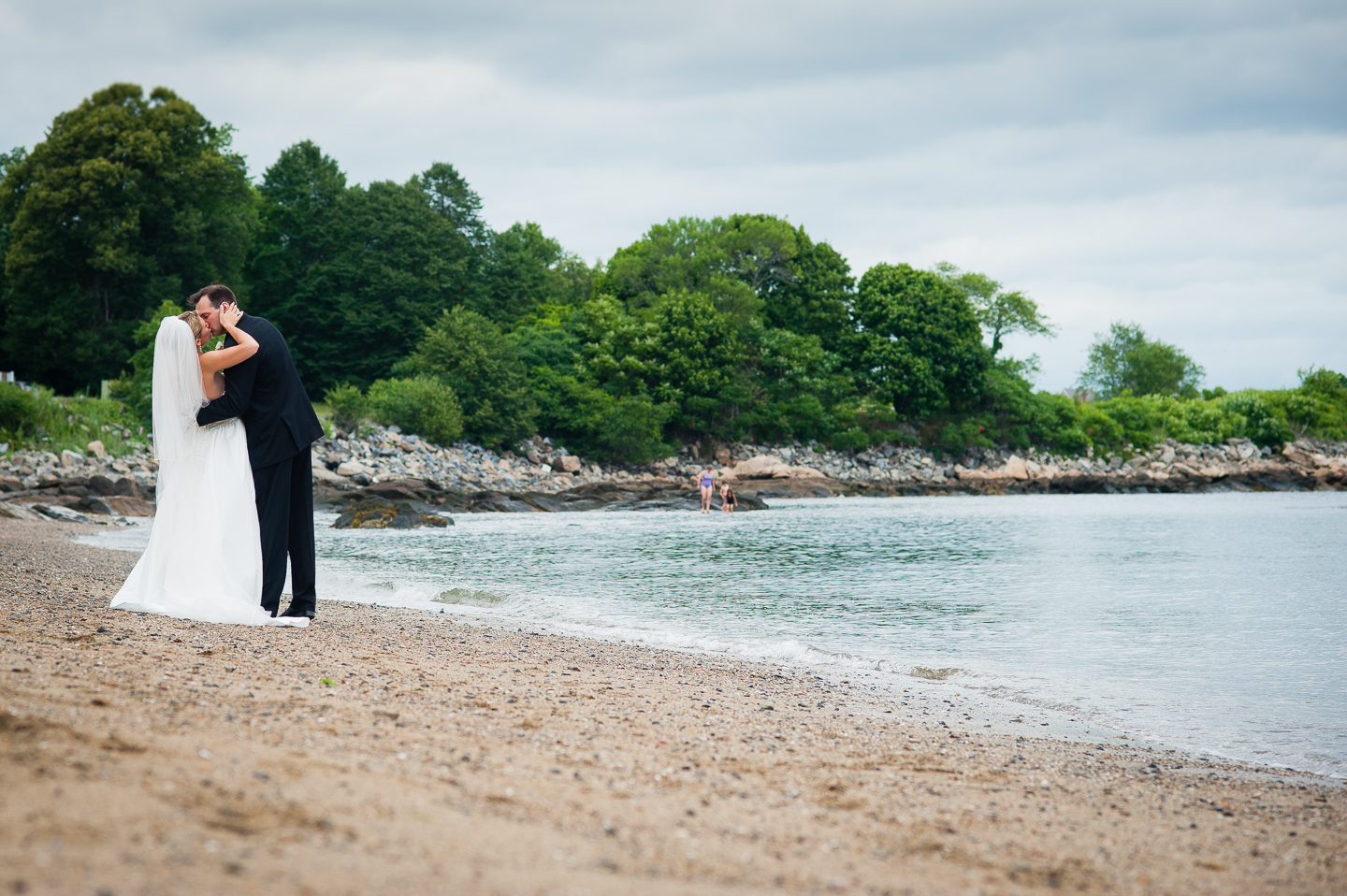 a bride and groom kiss by the ocean  with gorgeous trees behind 