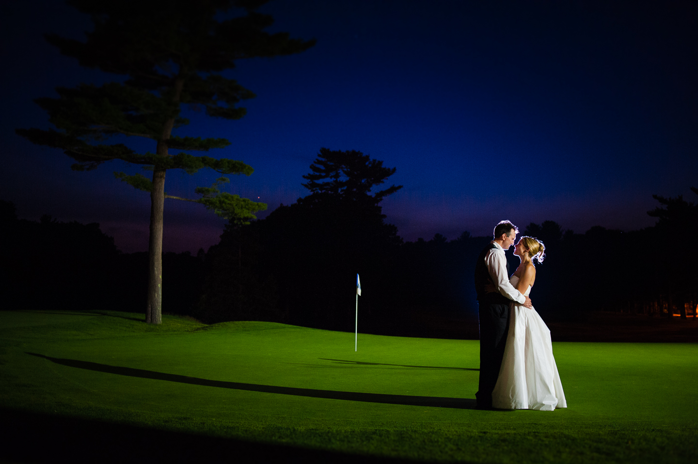 a bride and groom embrace for an end of the night photo on the lit up golf course 