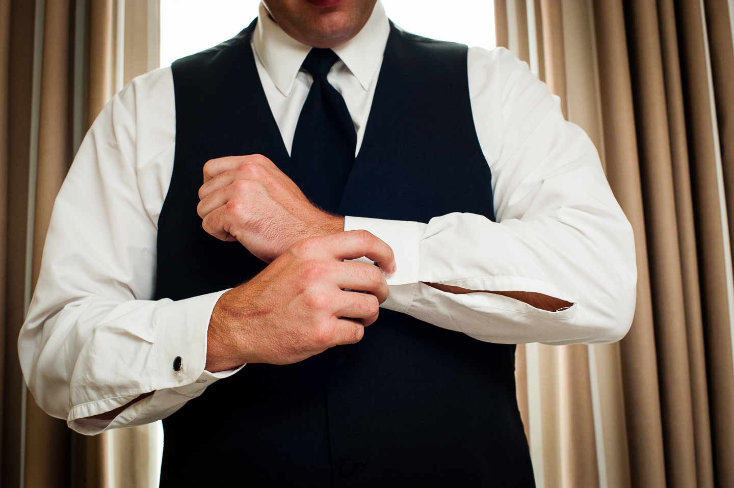 Groom putting on his cufflinks in front of big window