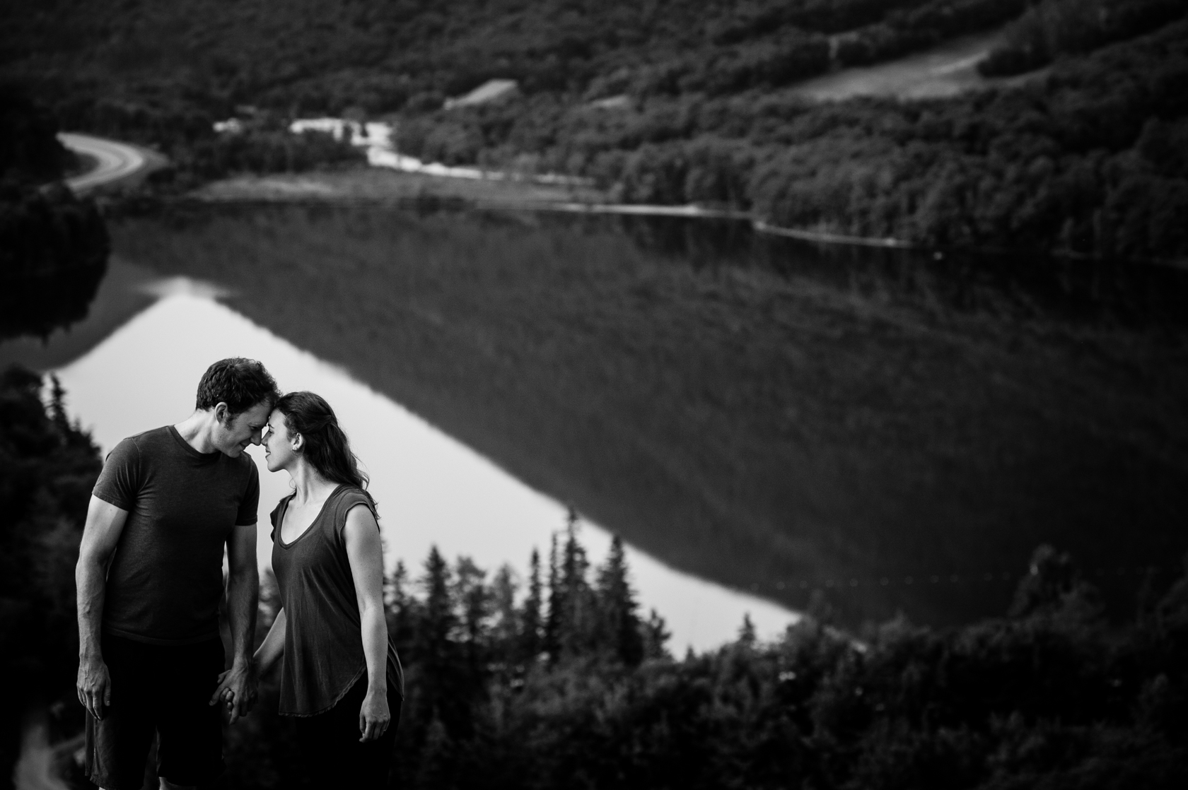 adventurous couple stands on mountain top with a mountain lake behind