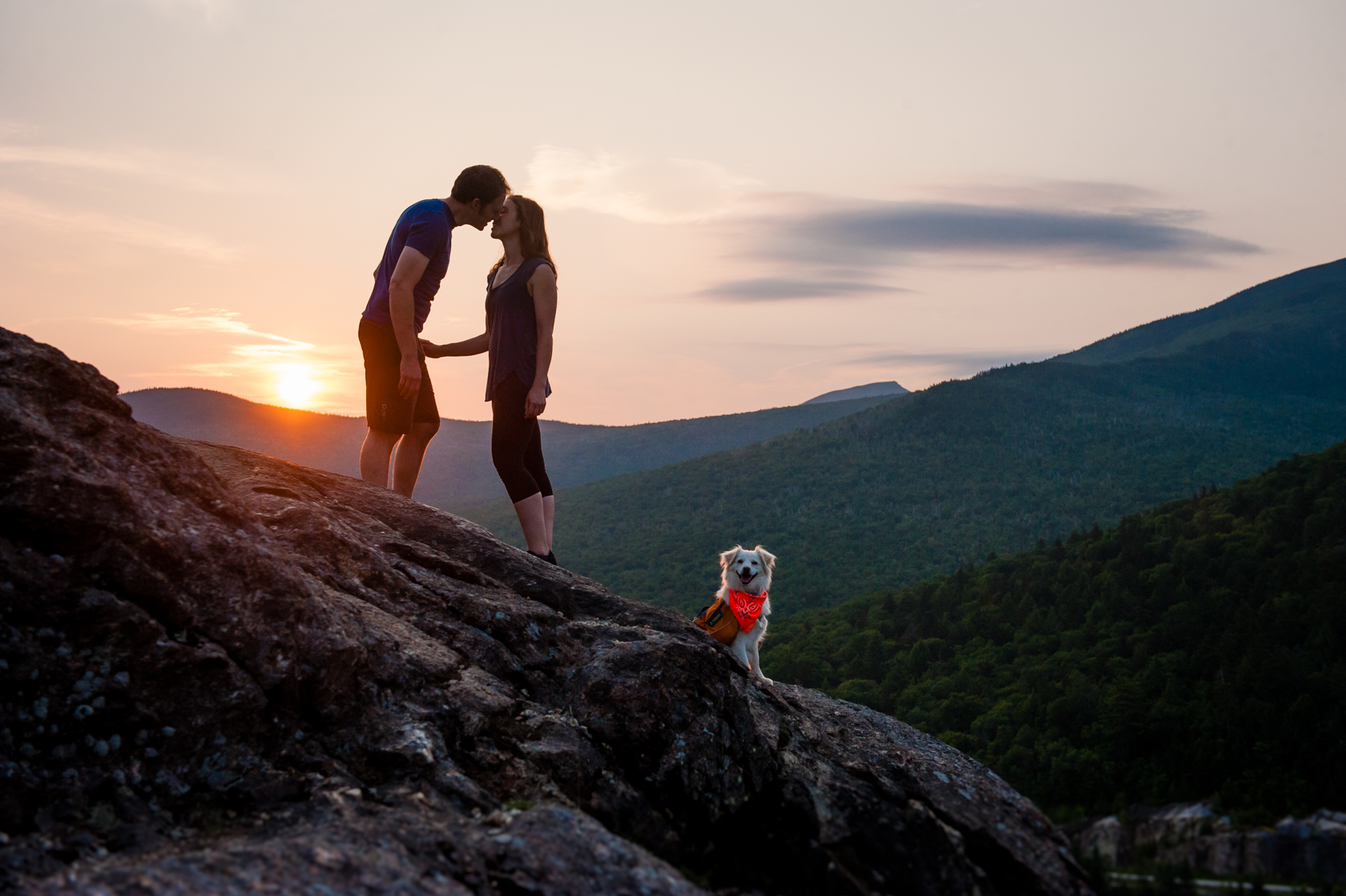 adventurous dog with his newly engaged owners pose on the edge of cliff  at sunrise