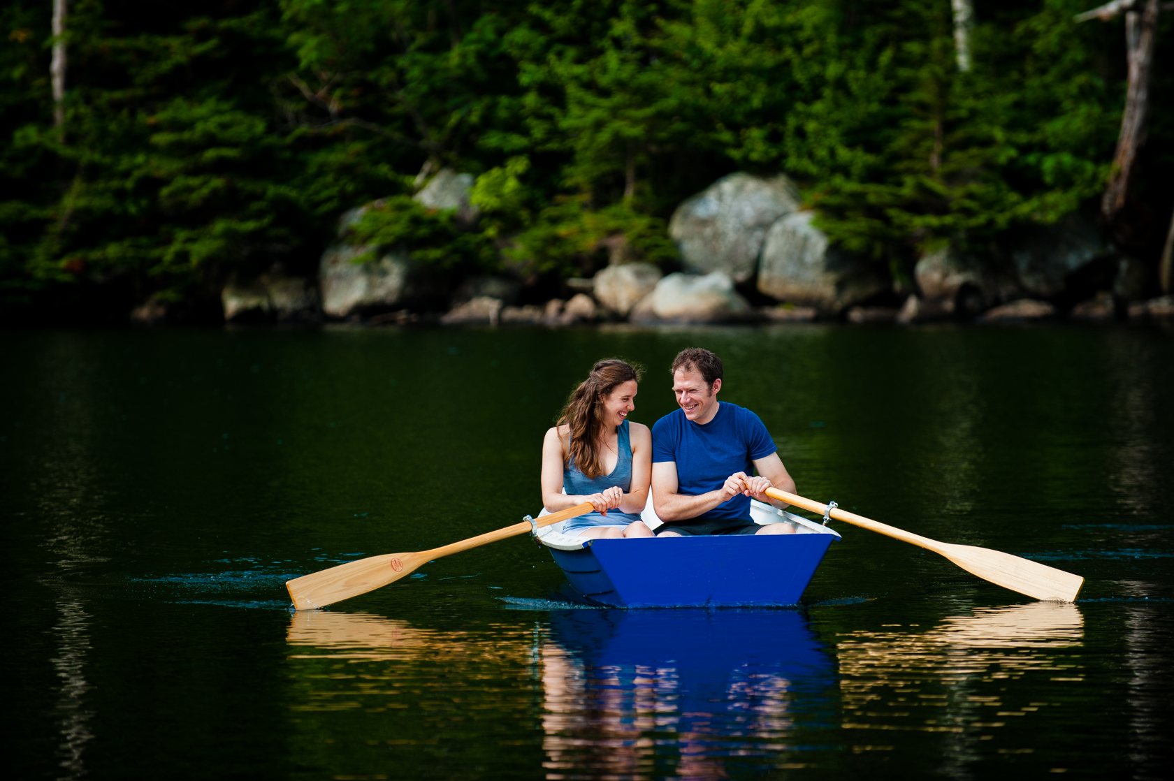 couple laughing as they row their boat on a mountain lake