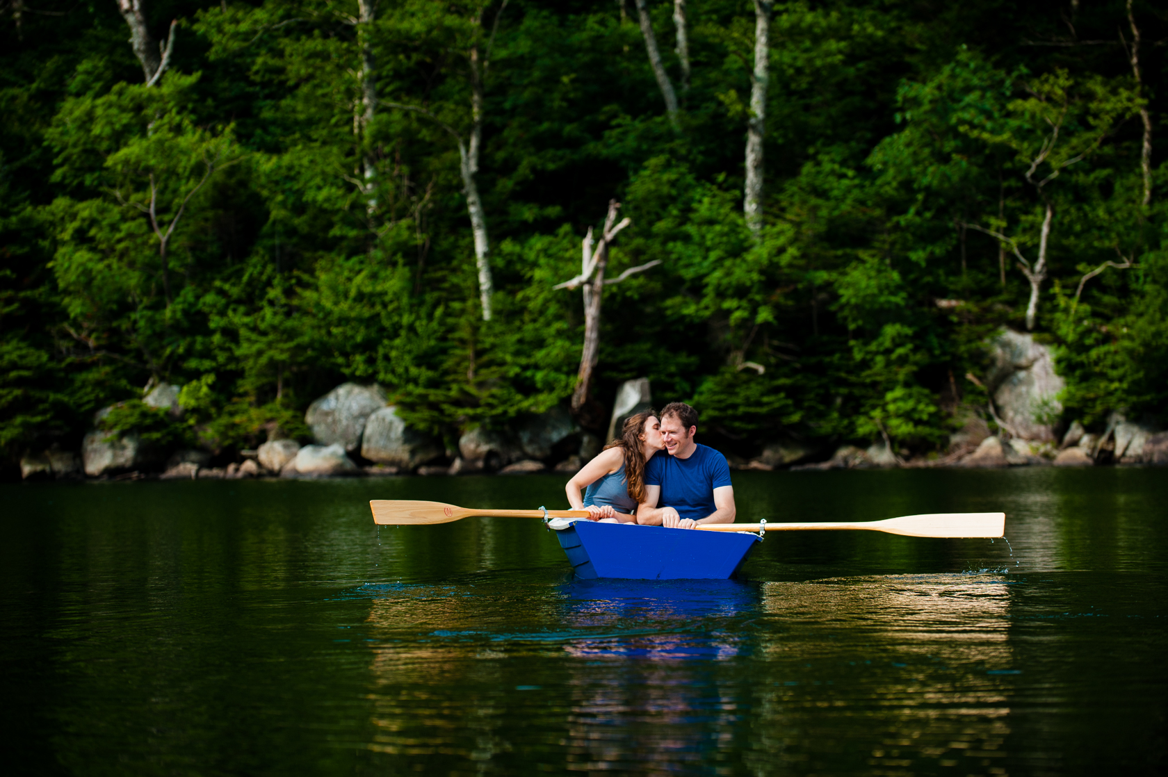 cute couple kisses in a row boat during their mountain lake adventure engagement session