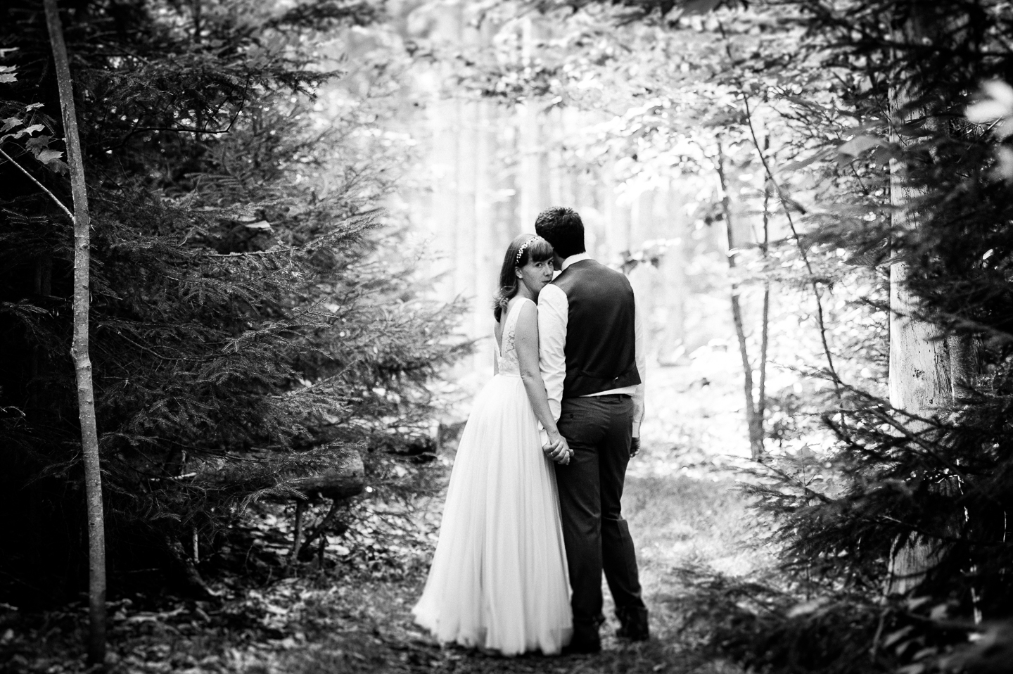 Beautiful bride looks over her shoulder standing next to her groom during their rustic woodsy wedding