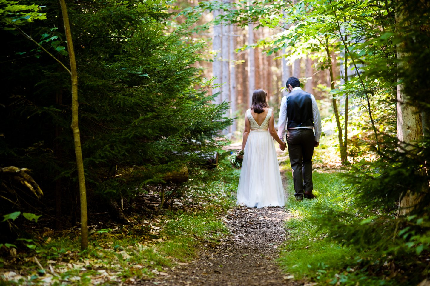 bride and groom hold hands and walk down beautiful wooded path