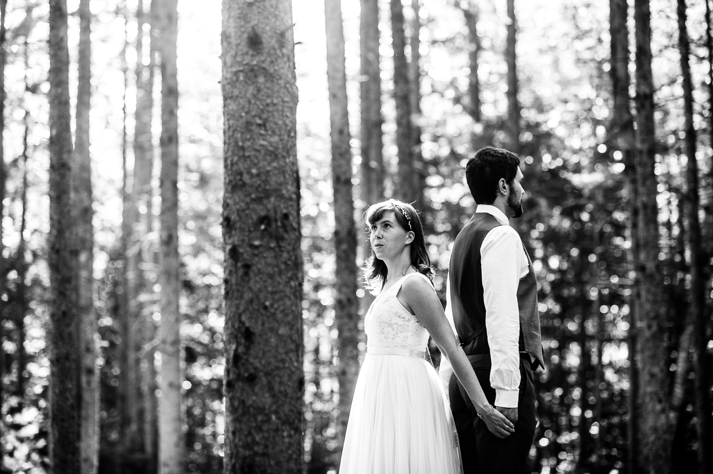 Bride and groom stands back to back holding hands in the middle of the woods