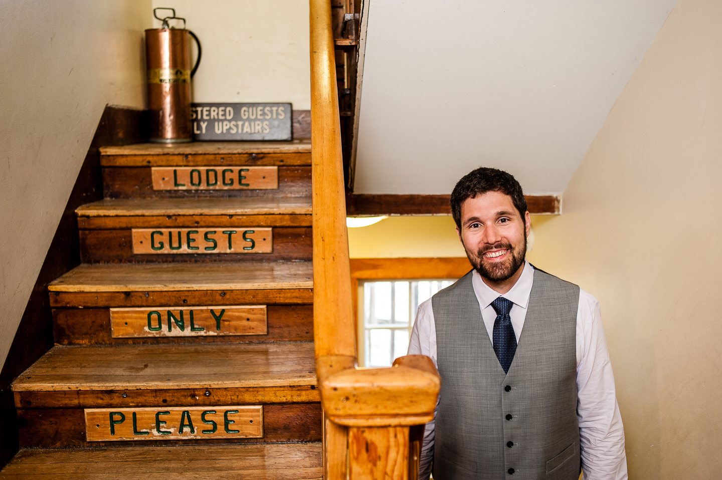 handsome groom stands on AMC Cardigan Mountain lodges staircase 