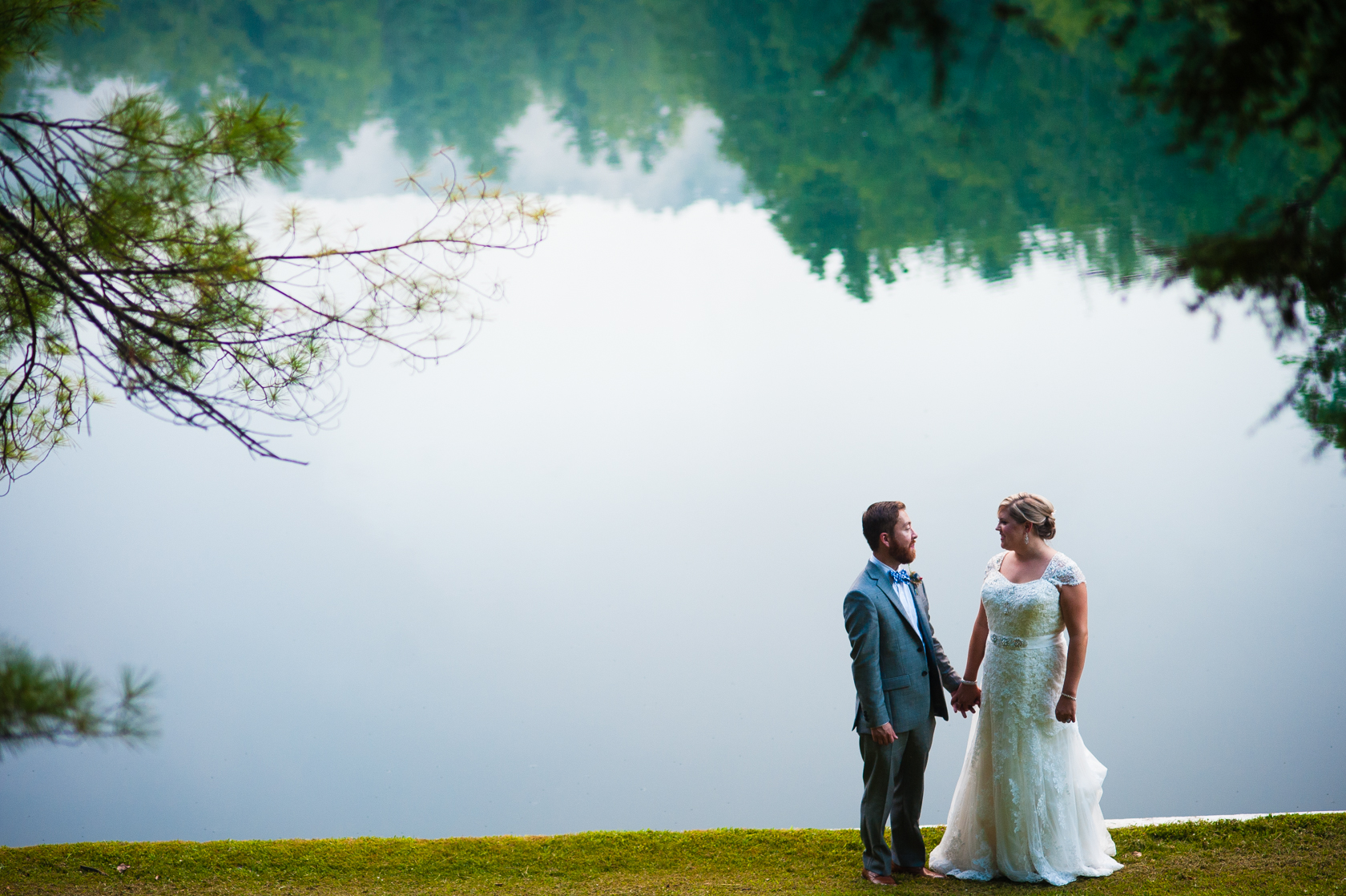 Bride and Groom hold hands with a beautiful misty lake behind during their mountain summer camp wedding 