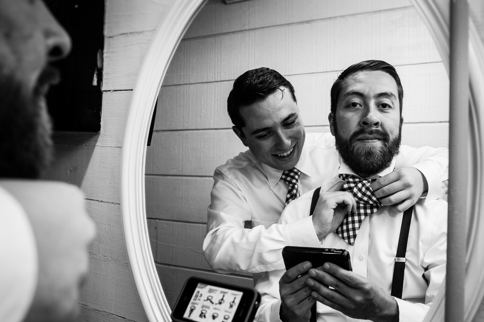 reflection of groom and his best man helping him tie his tie