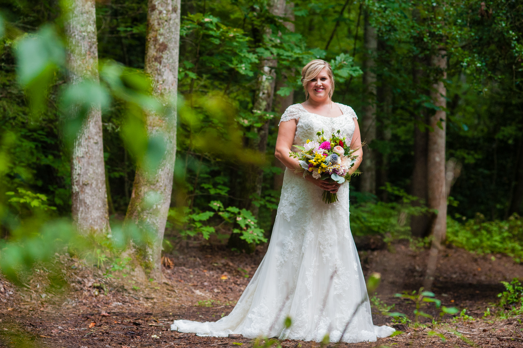 gorgeous bride holds her colorful bouquet on a wooded path 